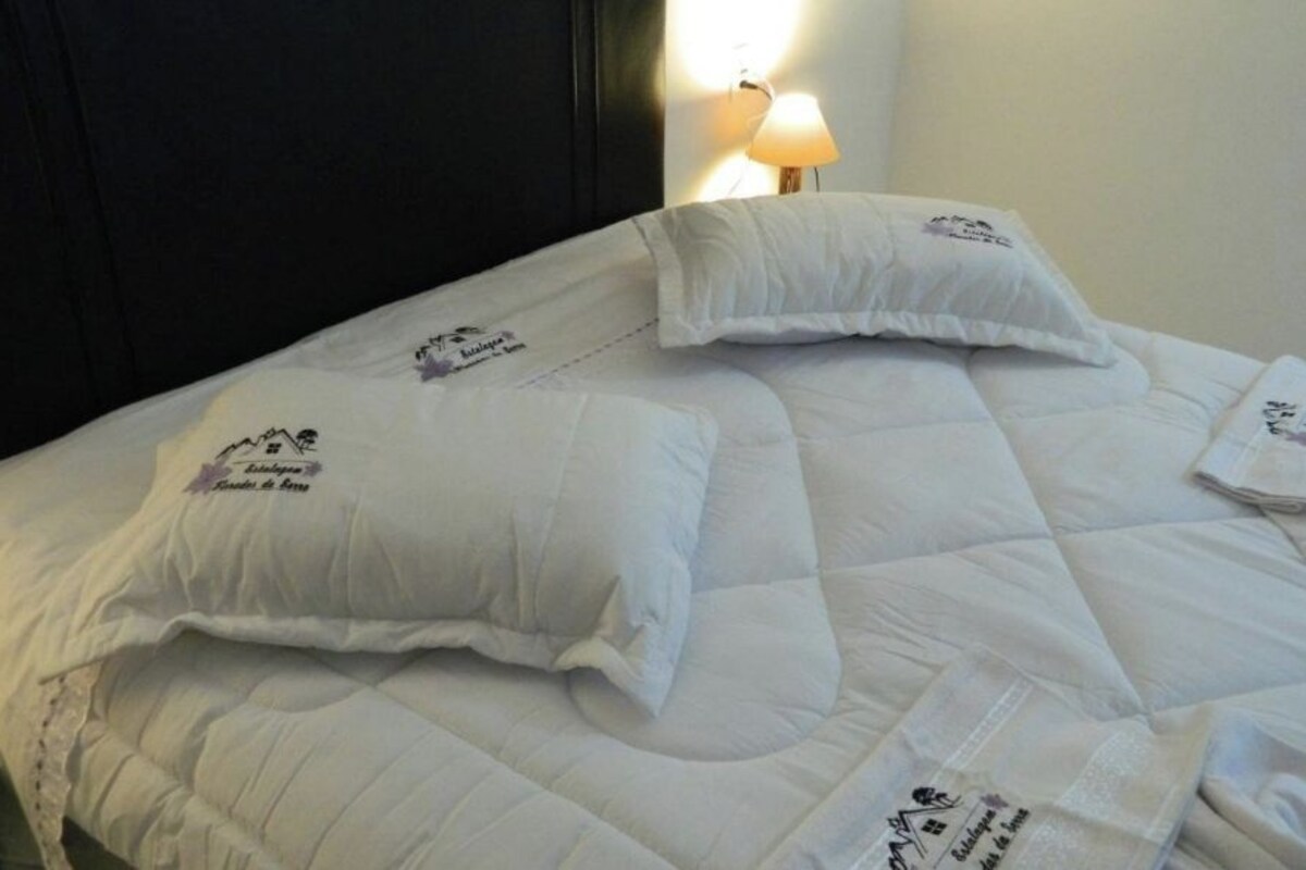 Una cama bien tendida con ropa blanca y almohadas, cada una con un logotipo y texto.