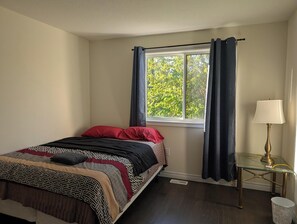 A bedroom with a bed, a window with curtains, a bedside table with a lamp, and a floor lamp.