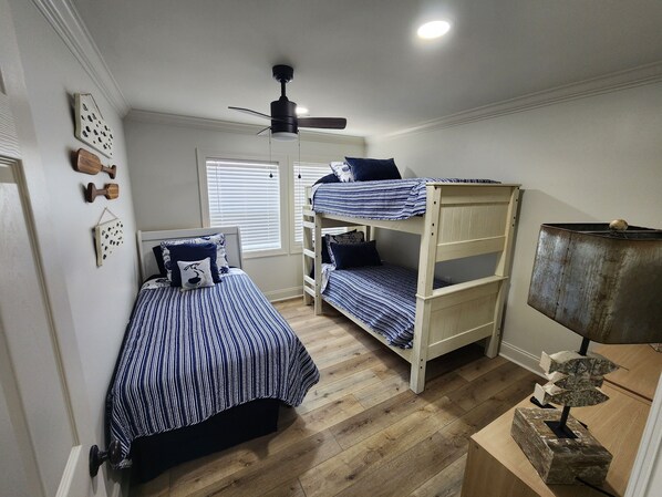 A room with a bunk bed, a single bed, a ceiling fan, and a lamp.