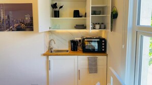 A compact kitchen with a built-in microwave, a sink, and open shelving above. - Studio Two (London)