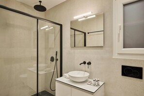 A modern bathroom with a glass shower enclosure, a white sink with a vessel basin, and a mirror above the sink. - Finders Akadimias Suites (Athens)