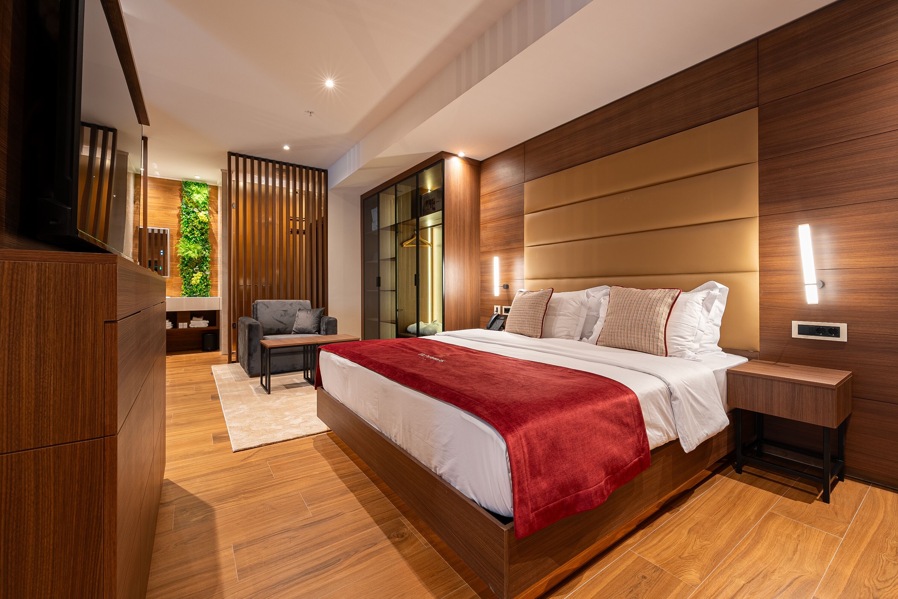 A modern bedroom with a large bed, wooden flooring, a seating area with a chair, and a built-in wardrobe.