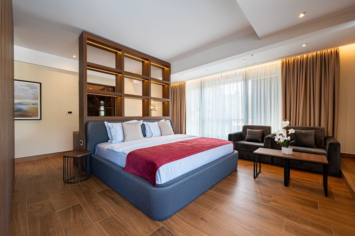 Una habitación de hotel moderna con una cama grande, un sofá, una mesita pequeña y una estantería empotrada.