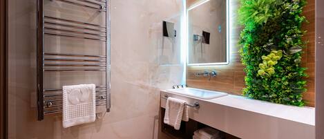Un baño moderno con cabina de ducha de vidrio, toallero cromado, lavamanos blanco y espejo con jardín vertical verde.