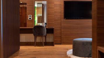 Una habitación moderna con un escritorio de madera, una silla gris, un televisor de pantalla plana en la pared y un pequeño reposapiés.