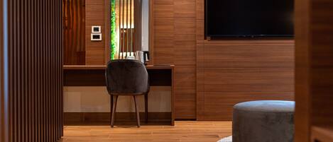 Una habitación moderna con un escritorio de madera, una silla gris, un televisor de pantalla plana en la pared y un pequeño reposapiés.