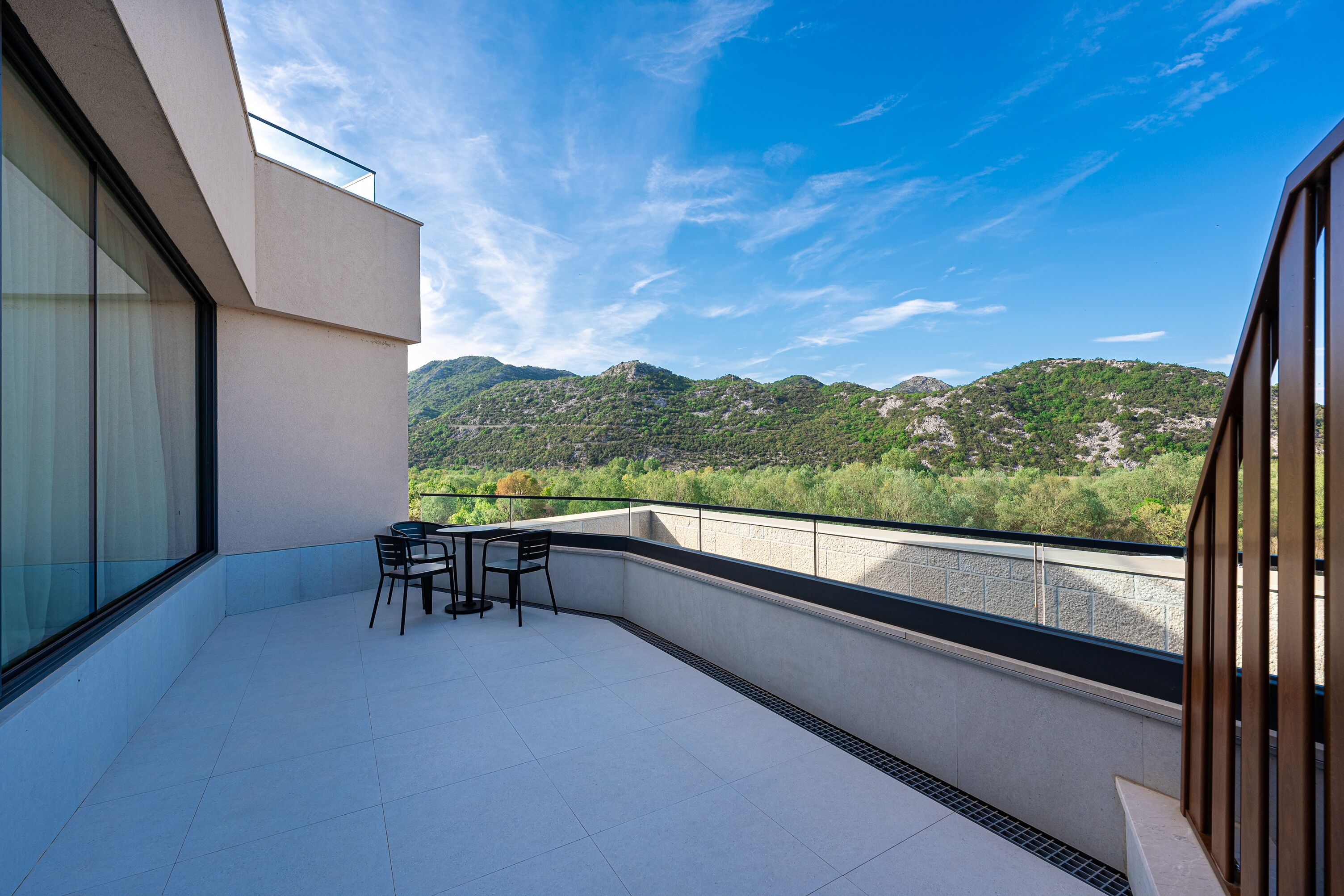 A balcony with a view of mountains and a dining area with chairs and a table.