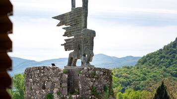 A stone statue of a figure with a flag on a rocky outcrop with a view of a forested mountain range in the background.