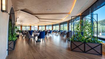 A spacious indoor dining area with wooden flooring, modern chairs, and large windows offering a view of the outdoors.