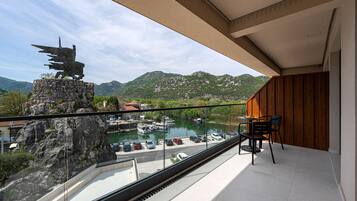 A balcony with a view of a marina, a statue, and a mountainous landscape.