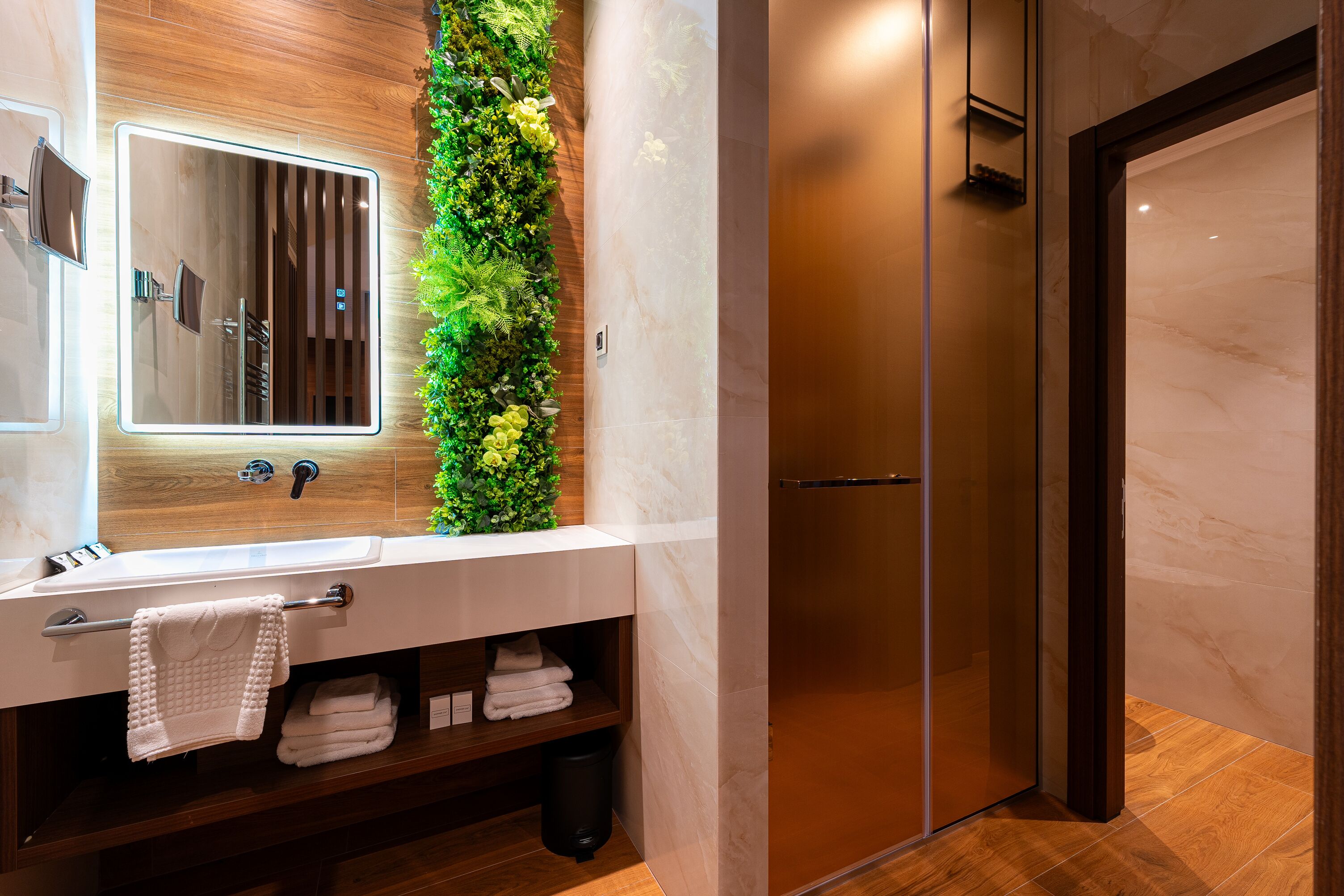 Een moderne badkamer met een houten wastafelmeubel, een grote spiegel, een verticale tuin en een douchecabine van glas.