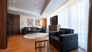 Una sala moderna con sofá, sillón y mesa de centro, piso de madera y un ventanal con cortinas traslúcidas.