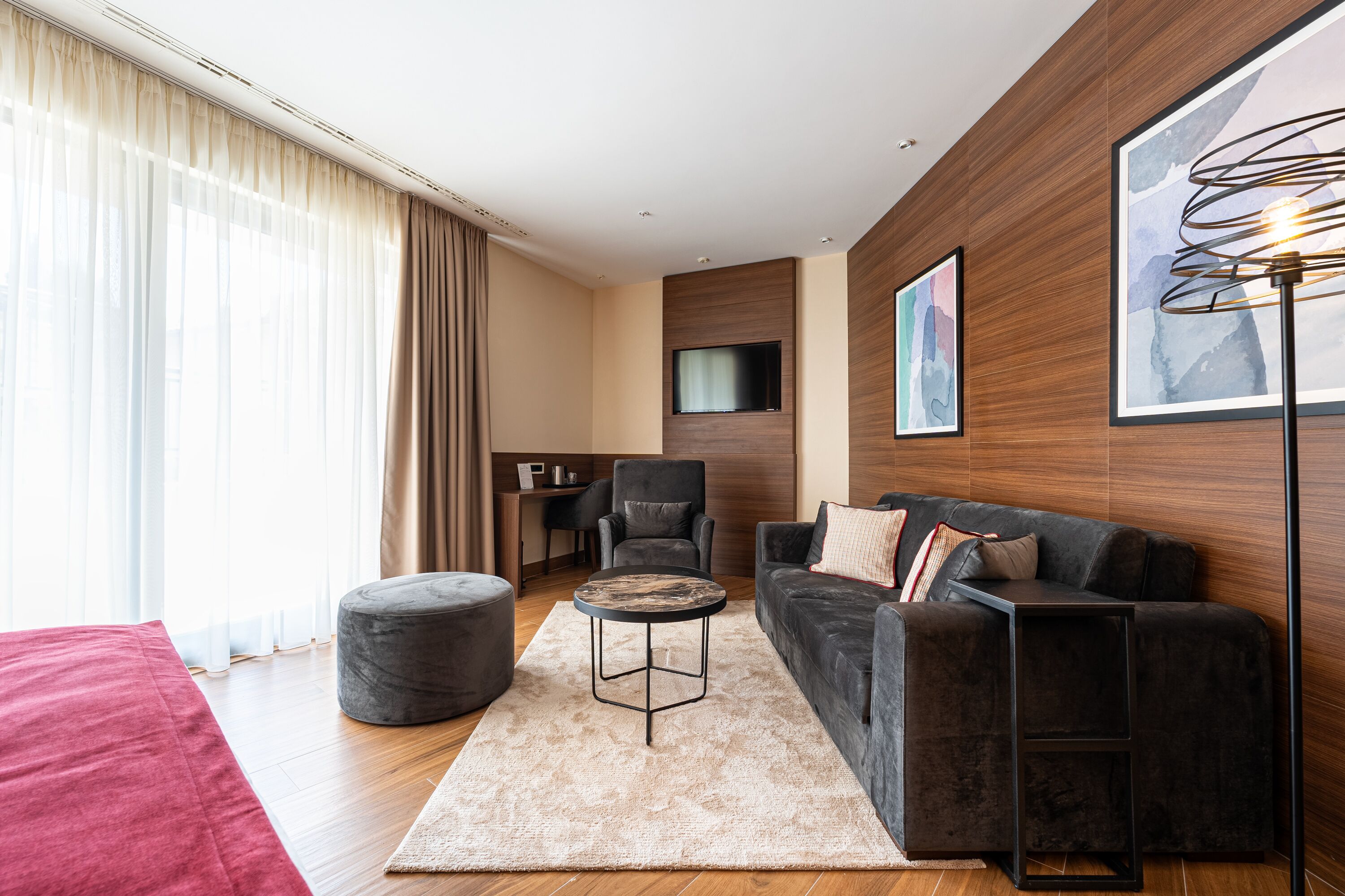 Una sala de estar moderna con un sofá, una mesa redonda de centro, un reposapiés gris y un televisor montado en la pared.