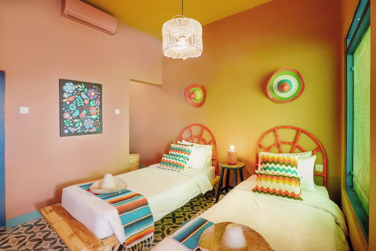 Una habitación con dos camas, una lámpara colgante, un cuadro en la pared y una pequeña mesa con una vela.