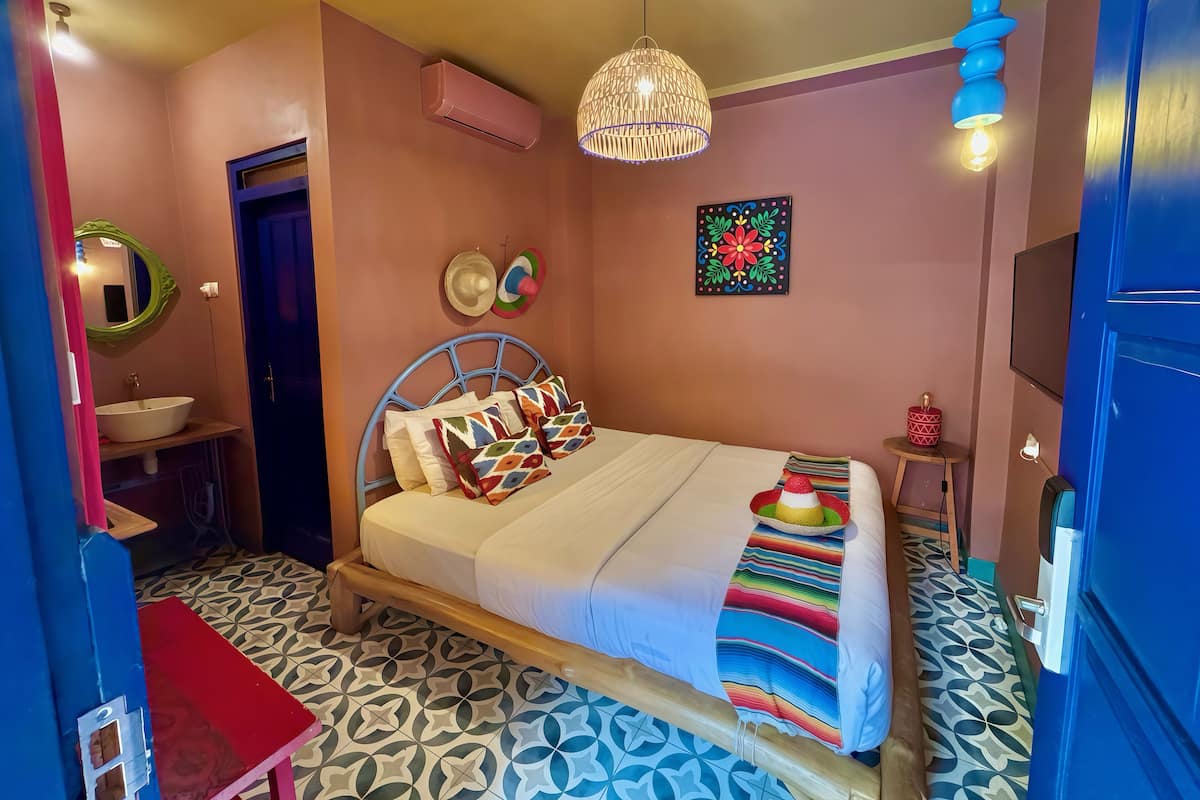 Un dormitorio con cama, mesita de noche, espejo, equipo de aire acondicionado, televisor montado en la pared y suelo estampado.