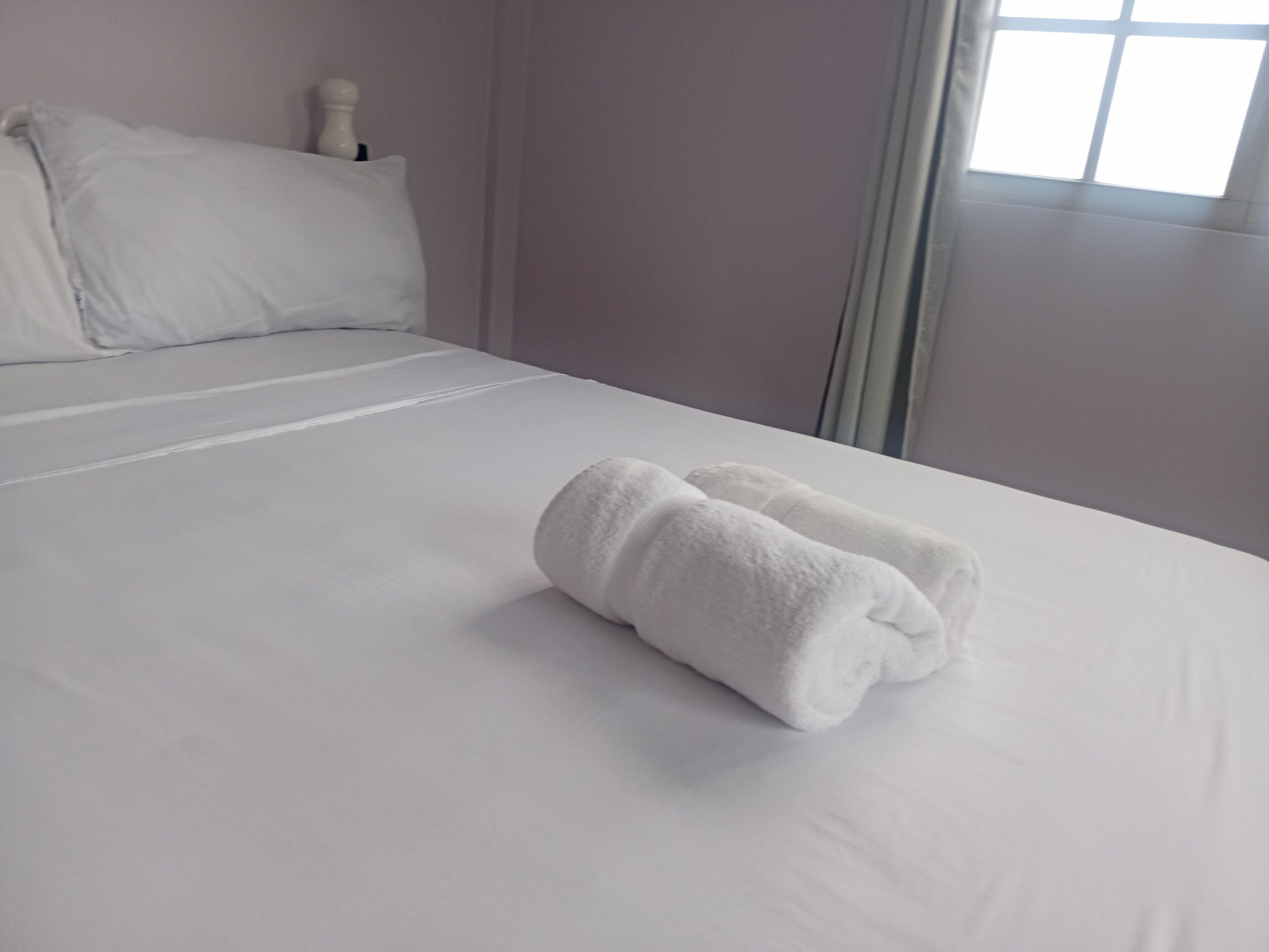 Una cama bien tendida con sábanas blancas y dos toallas enrolladas encima.