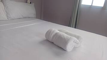 Una cama bien tendida con sábanas blancas y dos toallas enrolladas encima.