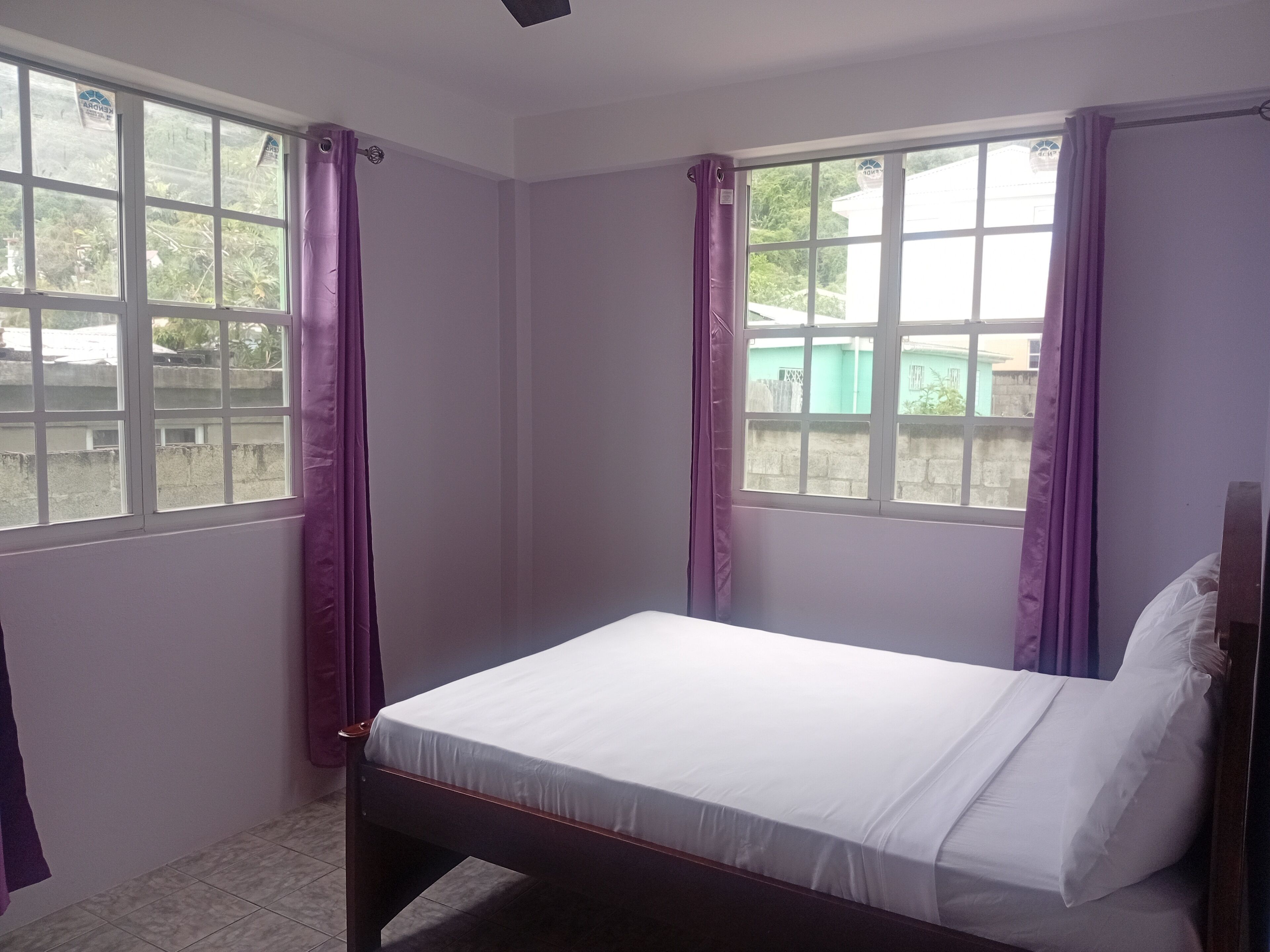 A single bed in a room with two windows, each with purple curtains.