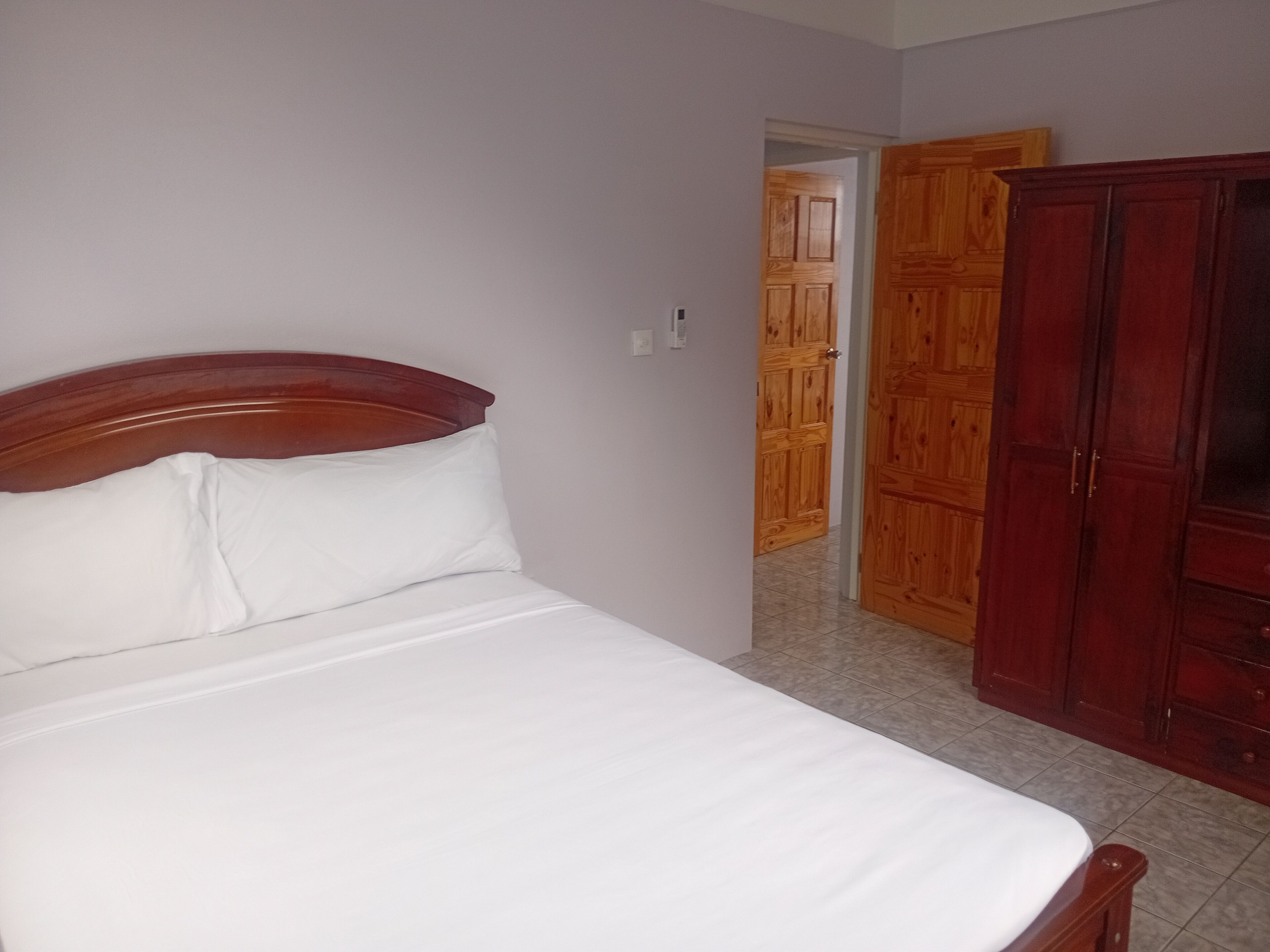 A bedroom with a single bed, wooden wardrobe, and a door leading to another room.