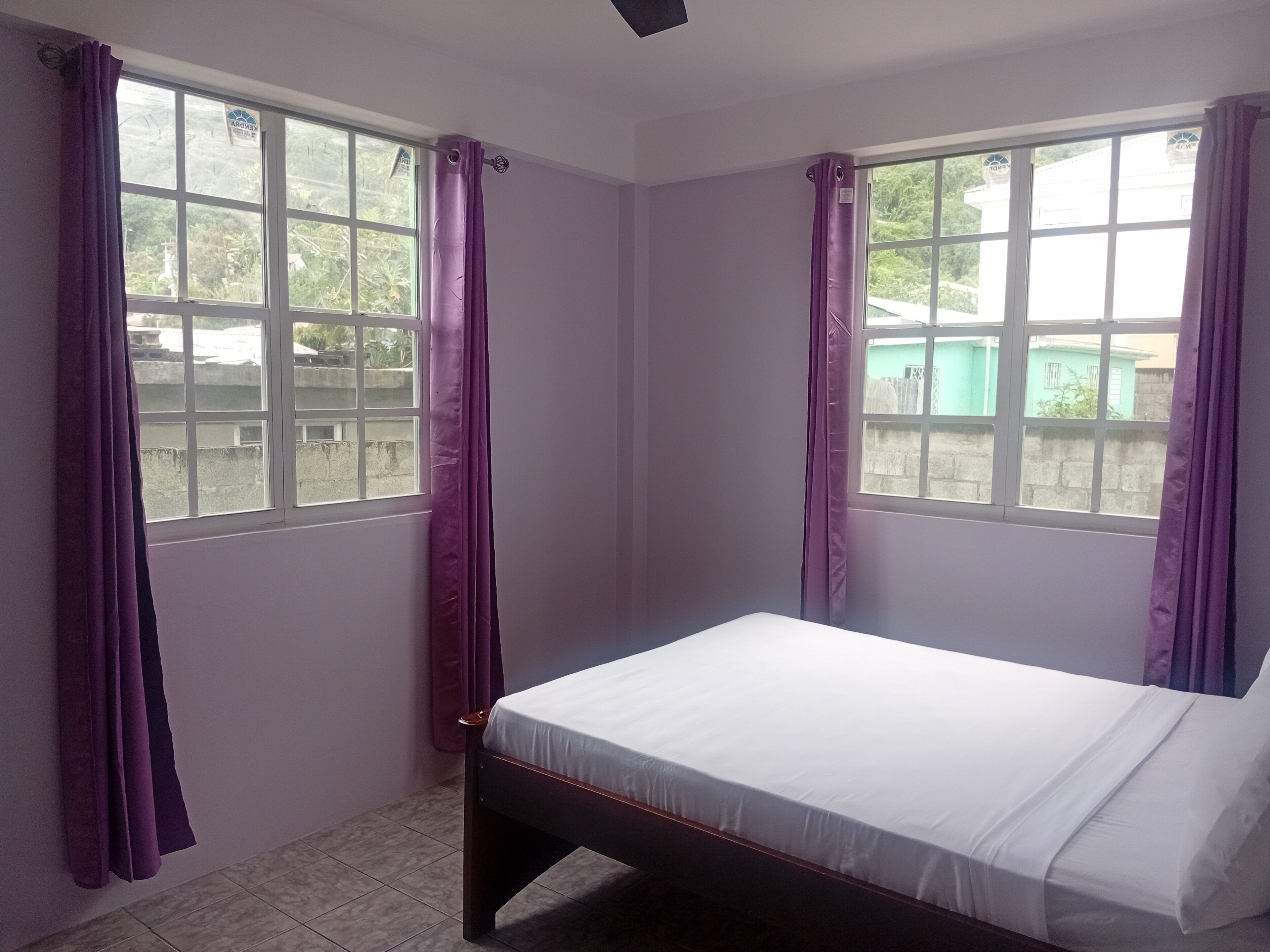 Une petite chambre avec un lit simple, deux fenêtres et des rideaux violets.