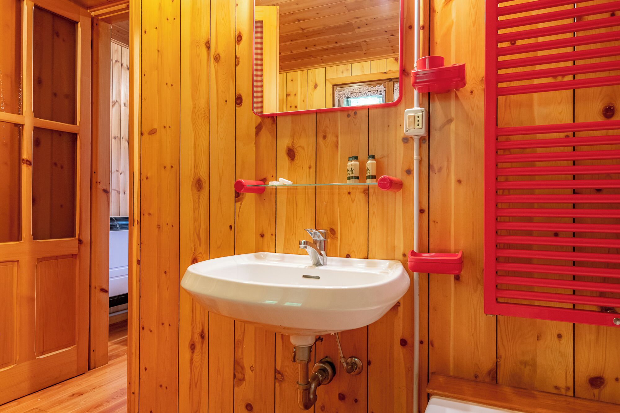 A wooden bathroom with a white sink, a mirror, and a shelf with toiletries.