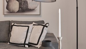 A modern living room with a grey sofa, a black floor lamp, a white candle, and a framed abstract painting on the wall. - Vision Stournari 65 (Athens)