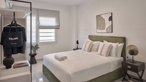 A modern hotel room with a neatly made bed, a bedside table with a lamp, a wall art piece, and a hanging bag labeled "TRUNK". - Vision Stournari 65 (Athens)