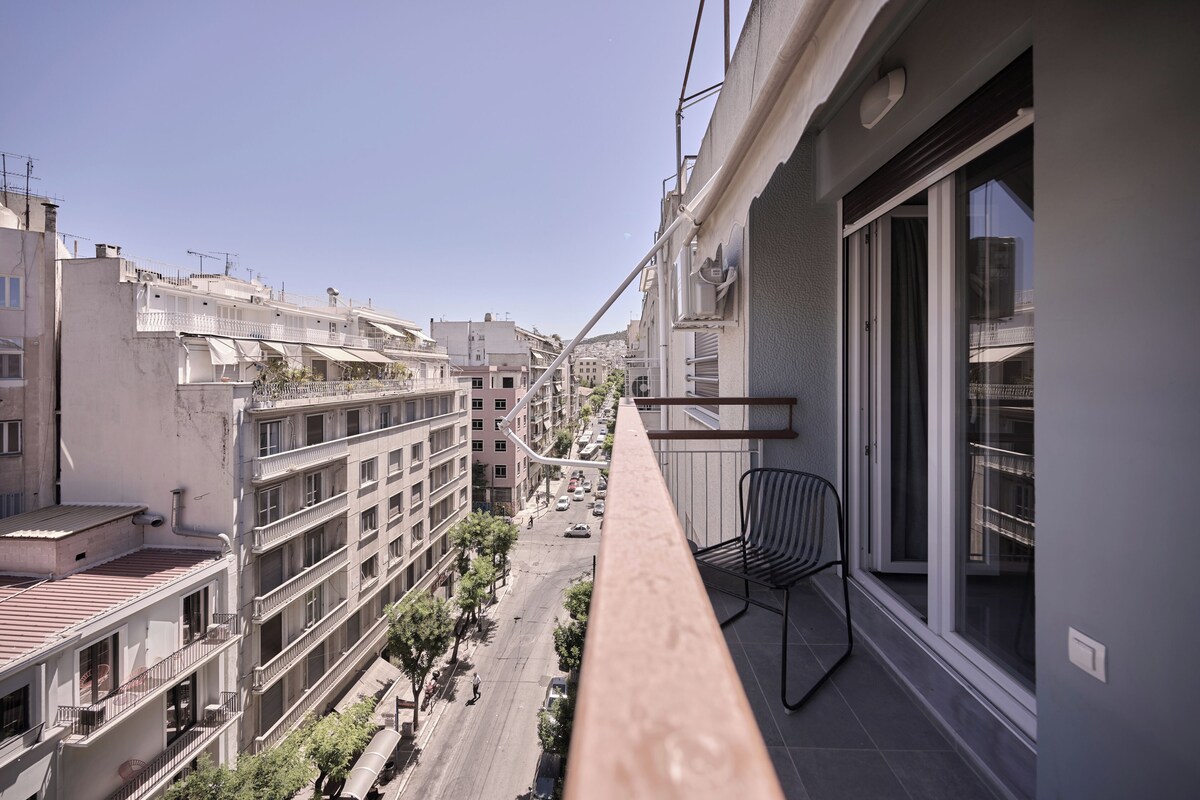A balcony with a view of a city street, a chair, and a window with a curtain.
