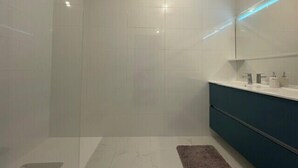 Une salle de bain moderne avec une douche à l’italienne en verre, un meuble-lavabo blanc doté d’un meuble sombre, et un petit tapis sur le sol.