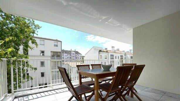 Un balcon avec une table et des chaises, des balustrades blanches et une vue sur les immebles.
