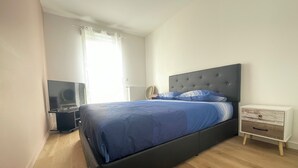 Une chambre à coucher avec un lit, une télévision, une table de chevet et une fenêtre avec des rideaux.