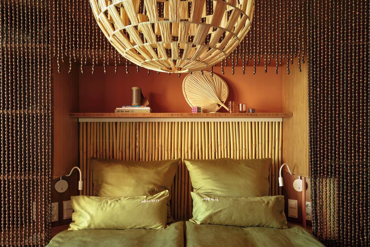 Une pièce comprenant un lit, un luminaire suspendu et une étagère avec des livres et un objet décoratif.