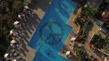 Vista aérea de un resort con una amplia piscina rectangular, tumbonas y sombrillas.