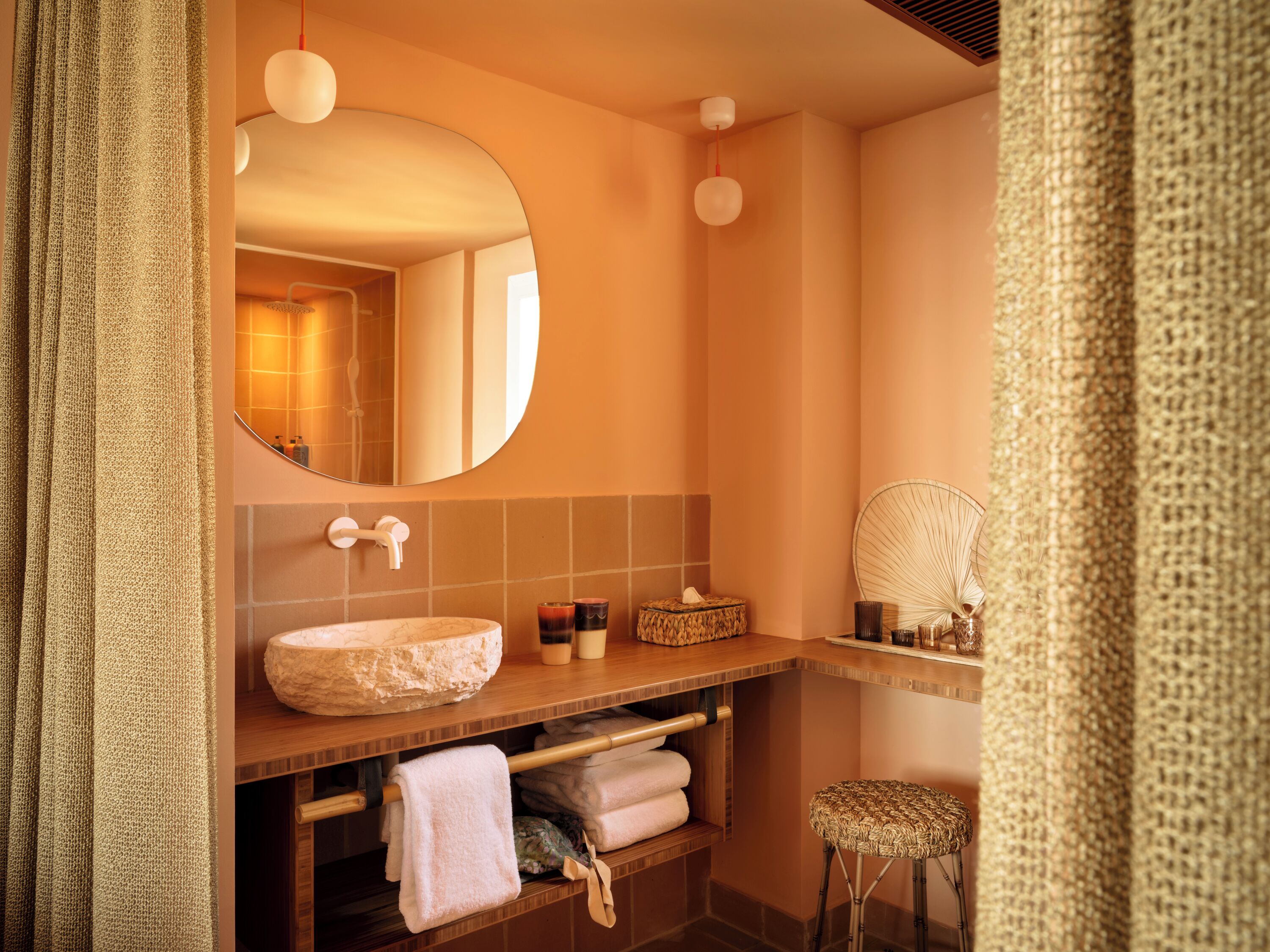 Une salle de bain avec un miroir rond, un lavabo et un tabouret.