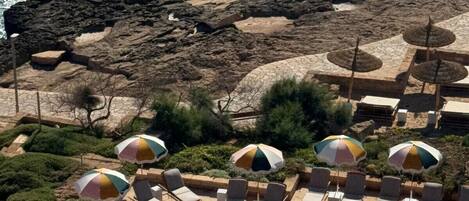 A poolside area with lounge chairs and umbrellas, overlooking a rocky coastline and the ocean.