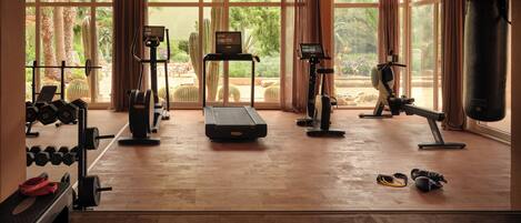 Un gimnasio espacioso con diversos equipos de ejercicio, amplias ventanas y vistas a un jardín.