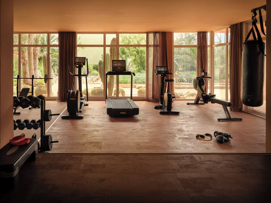Une salle de sport spacieuse, dotée de divers appareils d’exercice, de grandes fenêtres et offrant une vue sur un jardin.