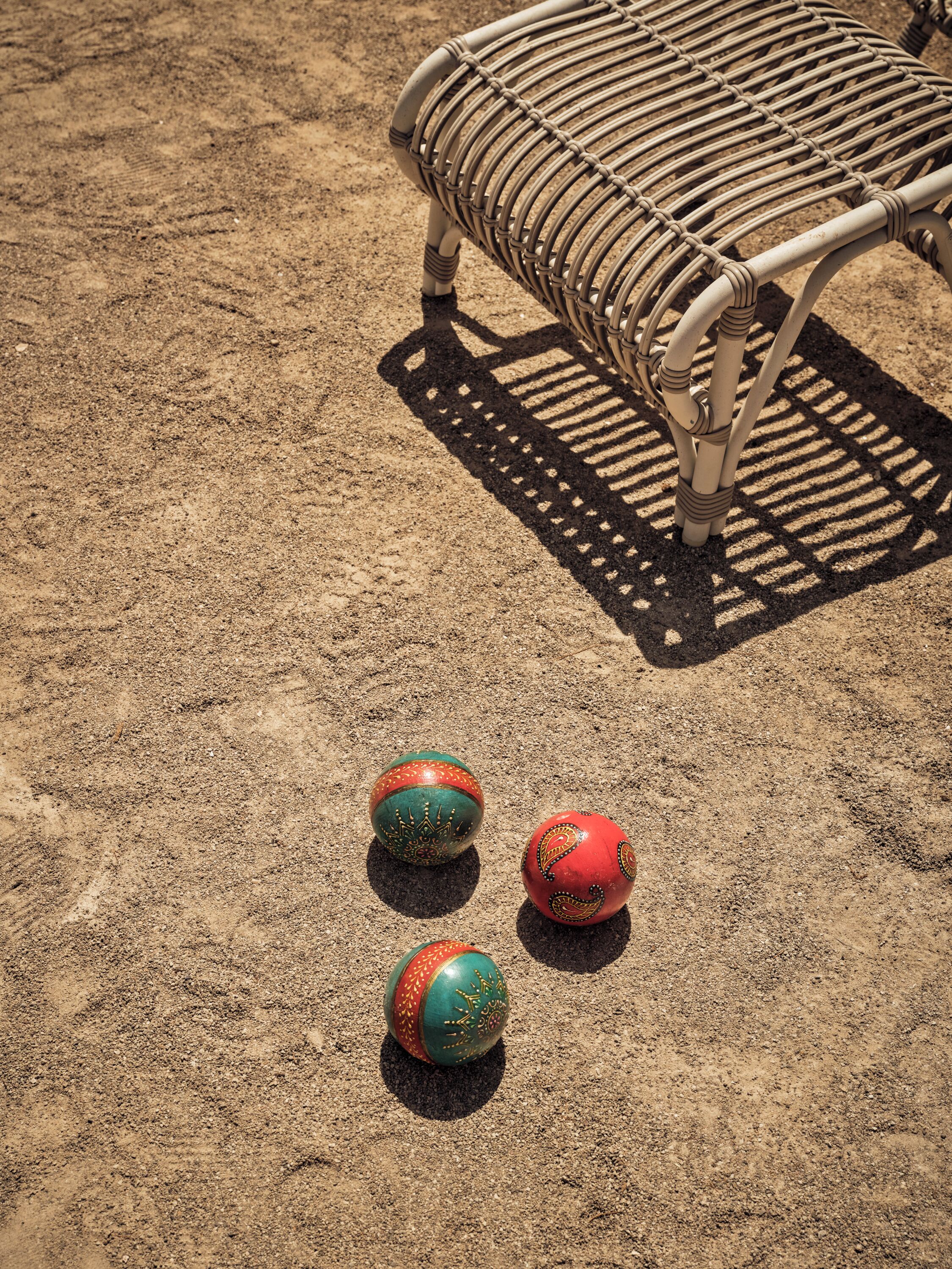 A wicker chair with a shadow on sandy ground.