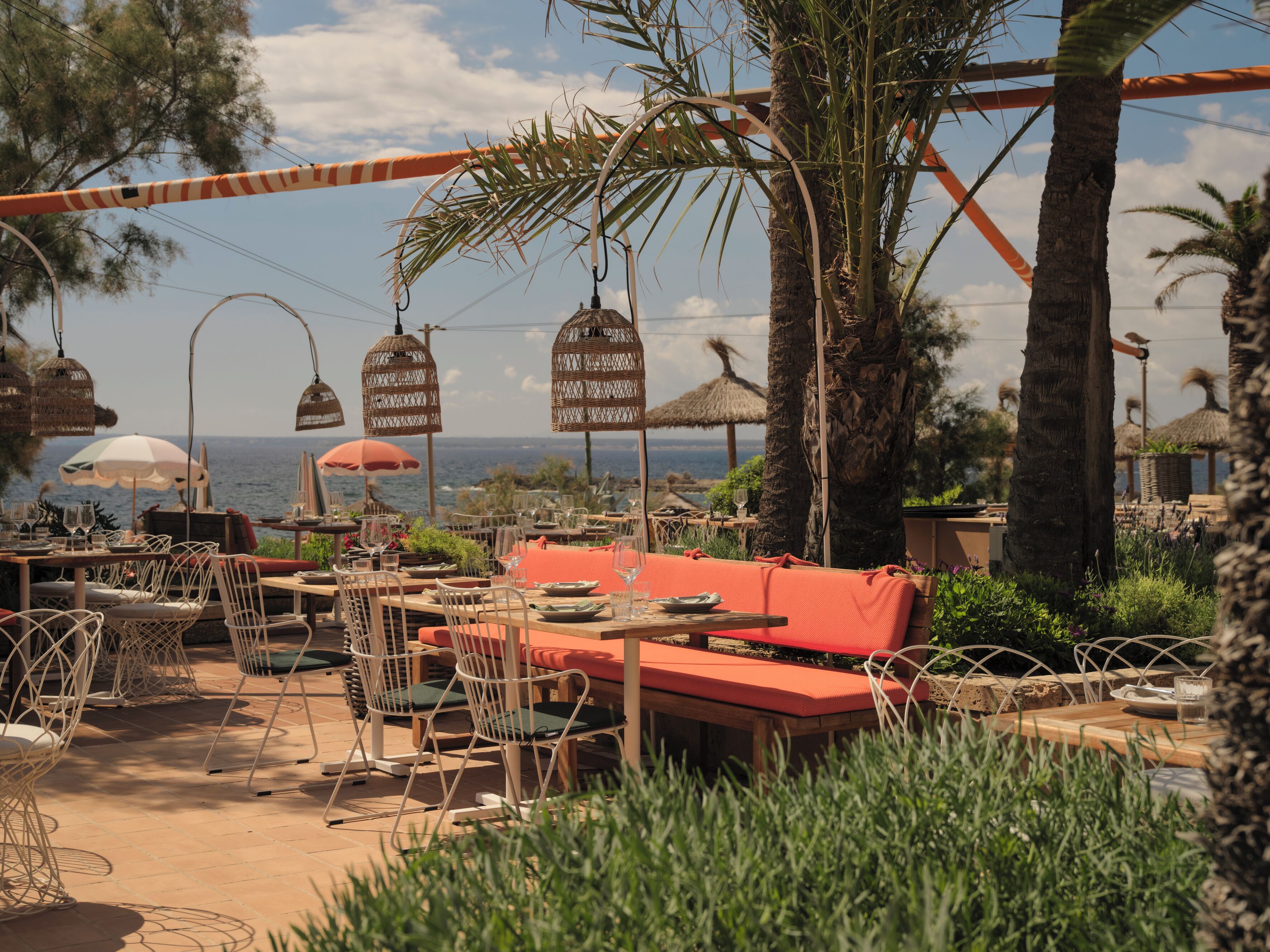 An outdoor dining area with tables and chairs, a red sofa, and hanging wicker lamps.