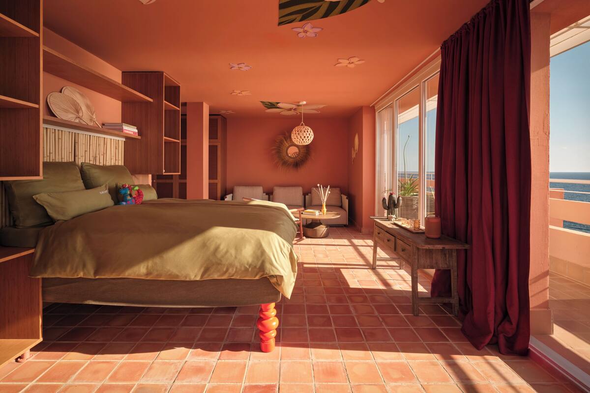 Une chambre à coucher avec un lit, un canapé, une petite table et une fenêtre avec des rideaux.