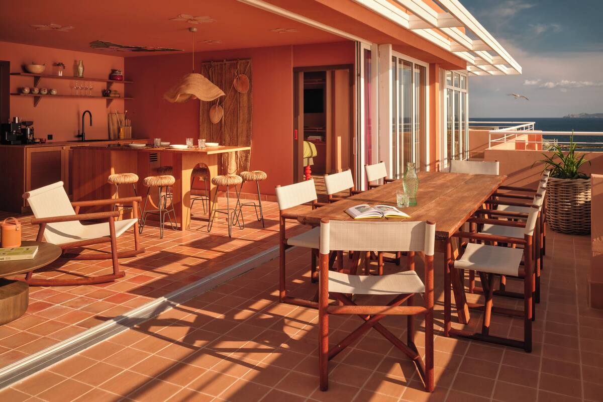 Un vaste espace extérieur aménagé pour les repas, avec une table et des chaises en bois, un coin bar et une vue sur la mer.