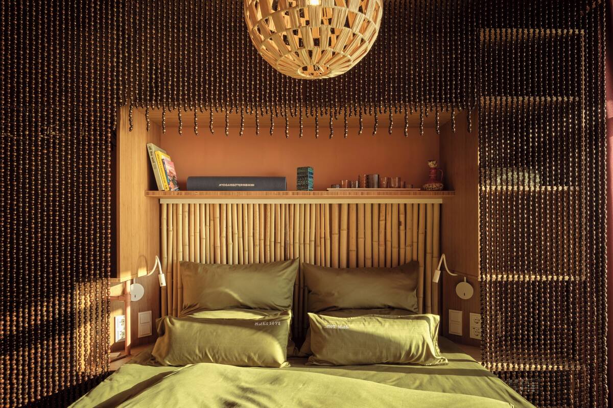 Une pièce comprenant un lit, une étagère avec des livres et un objet décoratif, ainsi qu’un mur orné de lattes de bambou verticales.