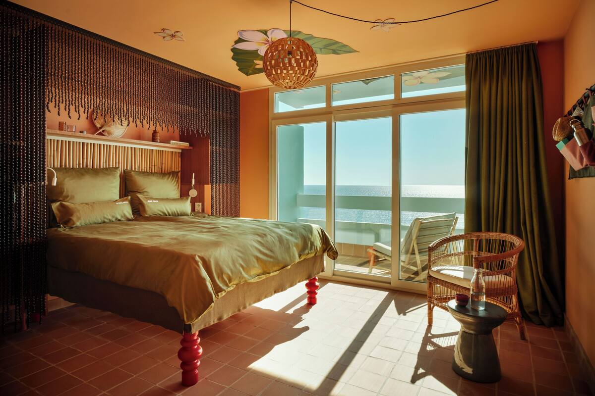 Une chambre avec un lit, une chaise, une table et une vue sur la mer.