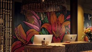Una recepción con dos portátiles, una silla tejida, una pared decorativa con un mural floral y una lámpara colgante.
