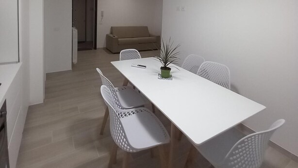 Een moderne eethoek met een witte tafel en stoelen, een potplant en een plafondlamp.