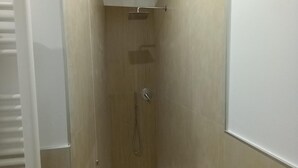 Een smalle, afgesloten douchecel met een witte vloer, een wand van verticale houten panelen en een witte handdoekhouder links.
