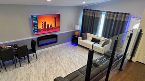 Een moderne woonkamer met een flatscreen televisie, een bank, een eethoek met stoelen en een glazen balustrade.