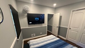 Een slaapkamer met een bed, een aan de muur bevestigde televisie, een deur en een raam met jaloezieën.