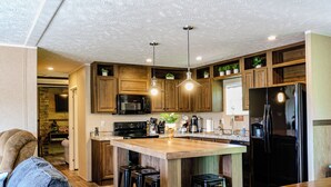 Eine moderne Küche mit Holzschränken, einer zentralen Kochinsel mit Barhocker, einem schwarzen Kühlschrank und Pendelleuchten.