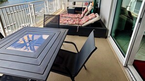 A balcony with a table and chairs, a sofa with cushions, and a view of the water and greenery. - The Wharf resort Orange Beach with Waterpark included (Orange Beach)